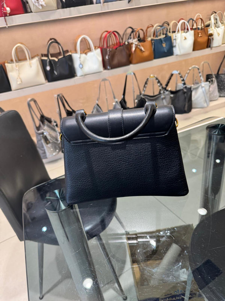 Black handbag on a glass display table with other bags in the background