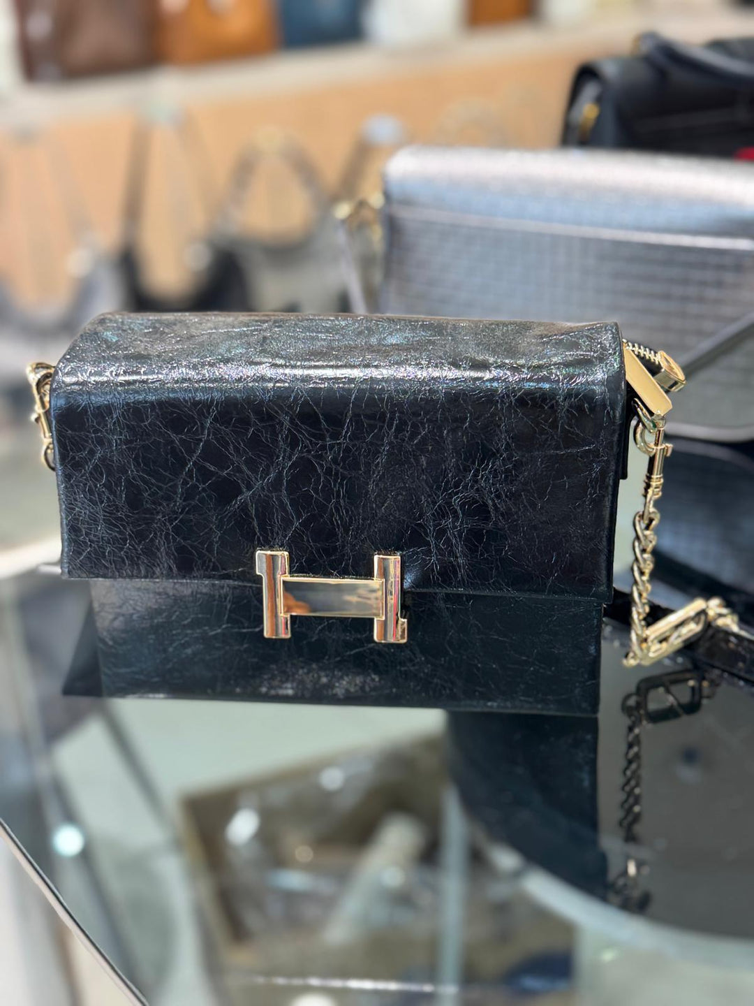 Black textured handbag with gold chain on a reflective surface