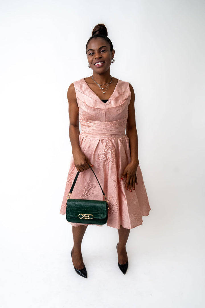 Woman wearing a pink dress holding a green handbag against a white background