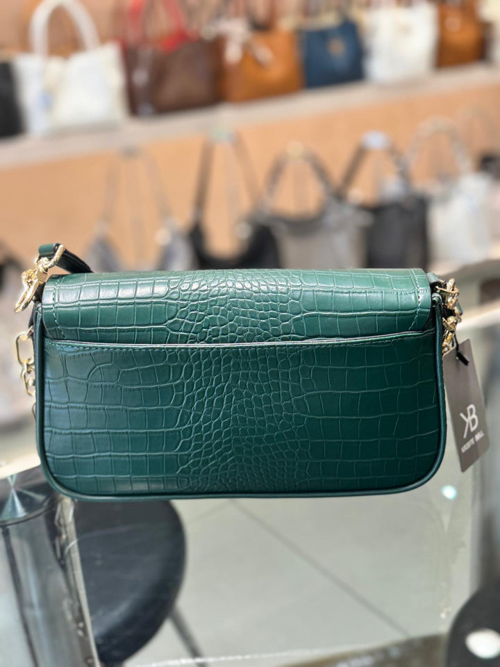 Green crocodile-patterned handbag with a visible brand tag on a reflective surface.