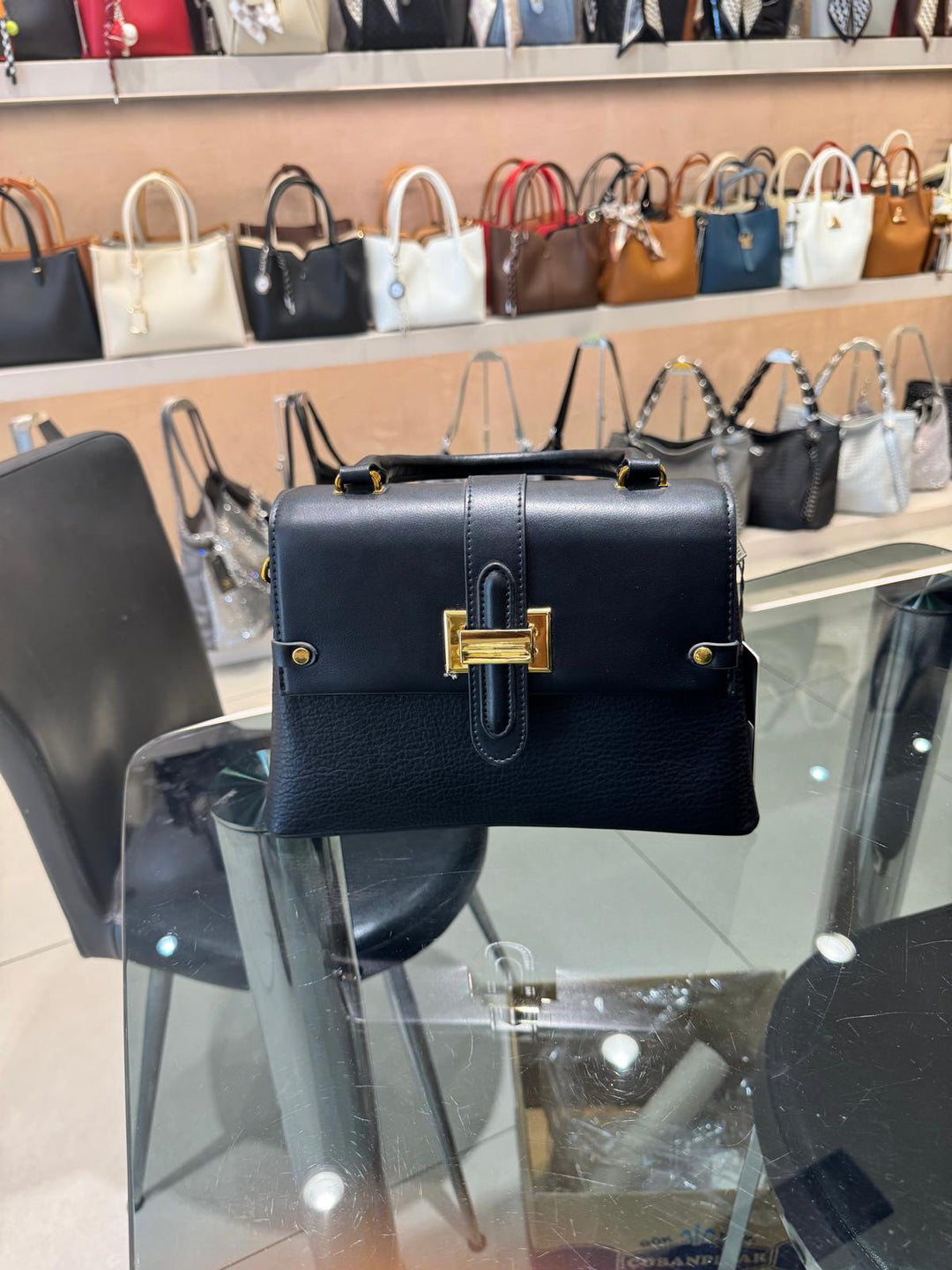Navy blue handbag with gold clasp on a glass table in a store setting with other bags in the background.
