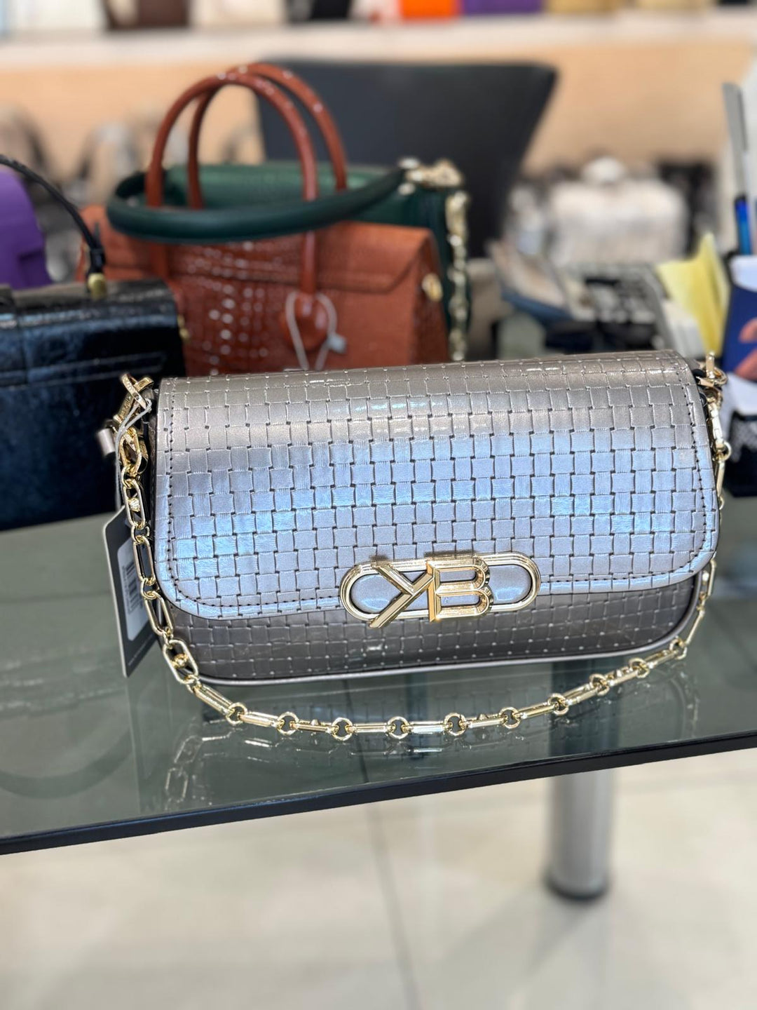 Silver handbag with gold chain on a glass surface, blurred background
